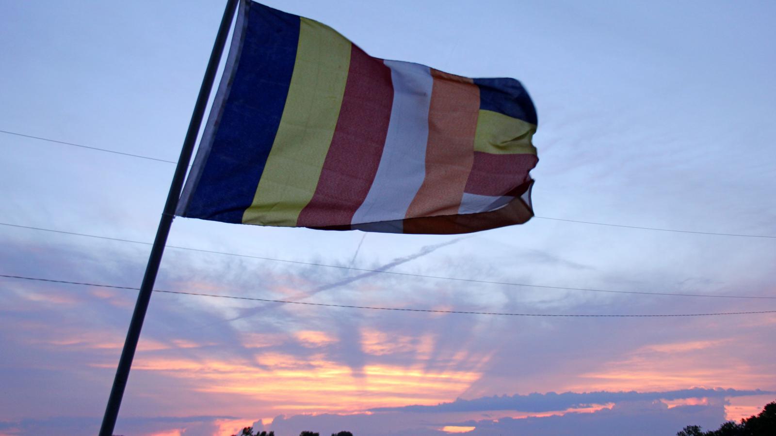 The Buddhist flag, created to symbolize and universally represent Buddhism, waves in the wind during sunset outside Wat Buddhasamakidham. 