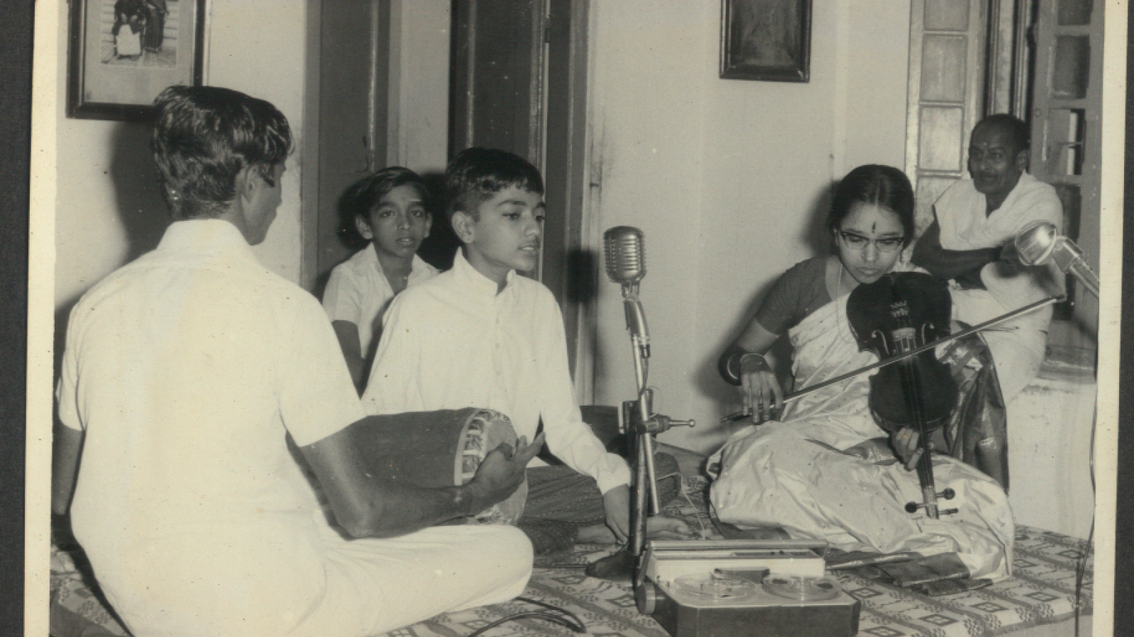 Photo of young Kannikeswaran singing into microphone while others, possibly his family, play instruments