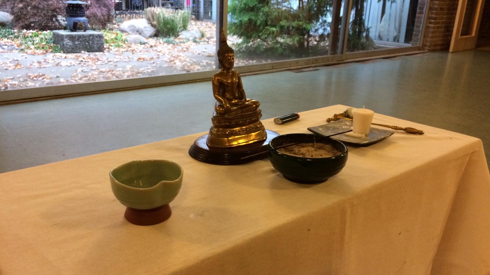 The Buddha altar with a statue of Buddha, incense, a candle and water