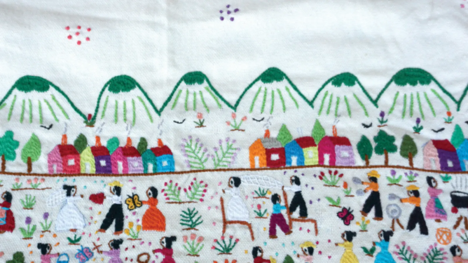 An embroidered folk art scene of dozens of people in a field in front of mountains