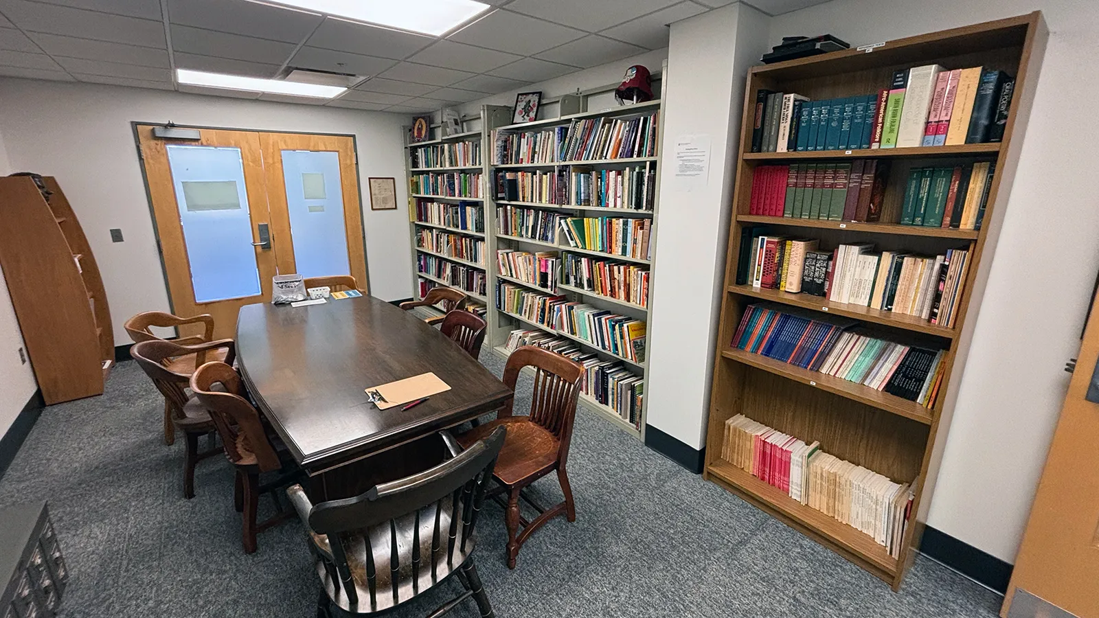 A large wooden table with chairs around it and bookshelves lining the walls of the surrounding room