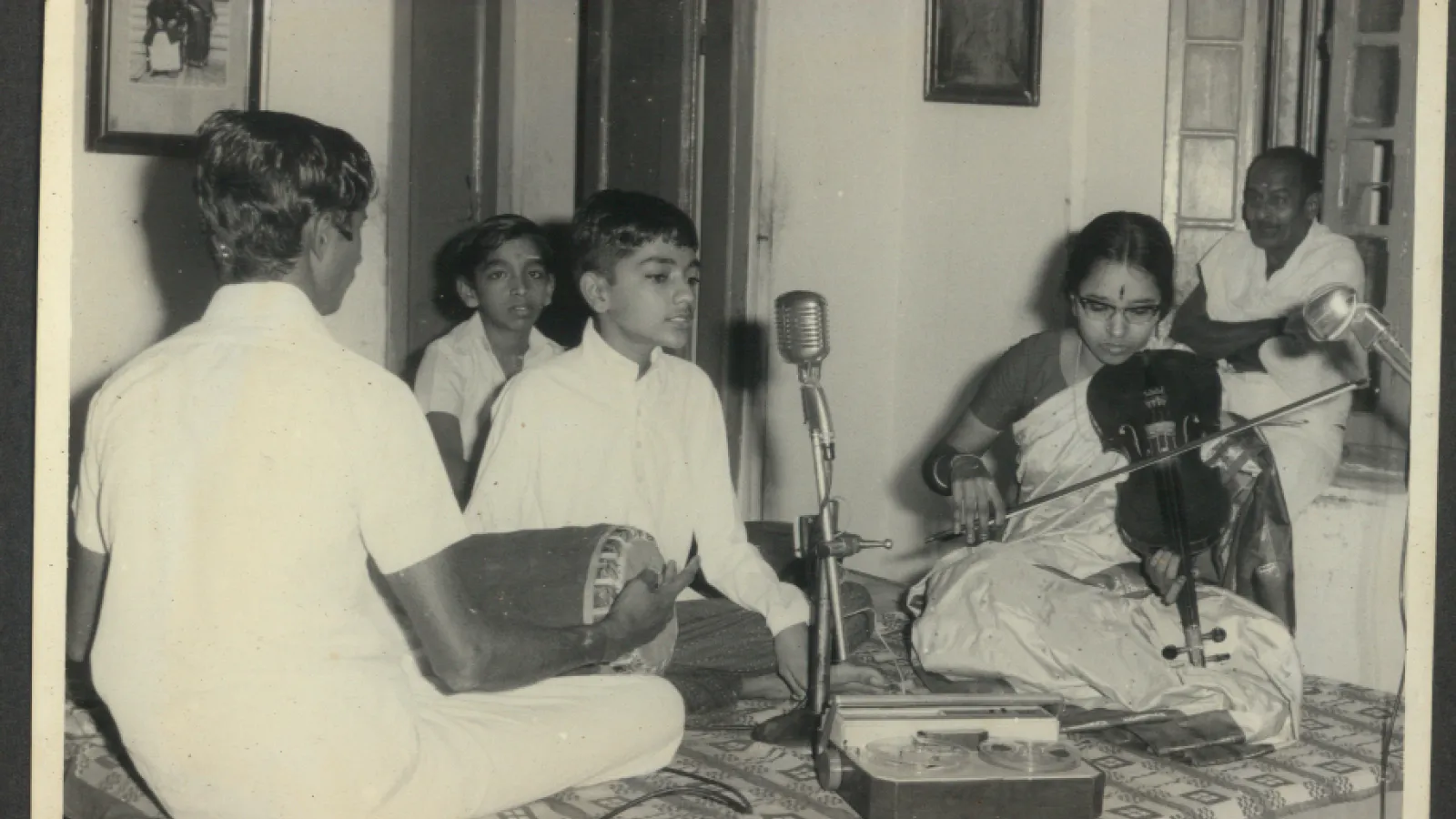 Black and white photo of young Kannikeswaran singing into microphone while others play instruments