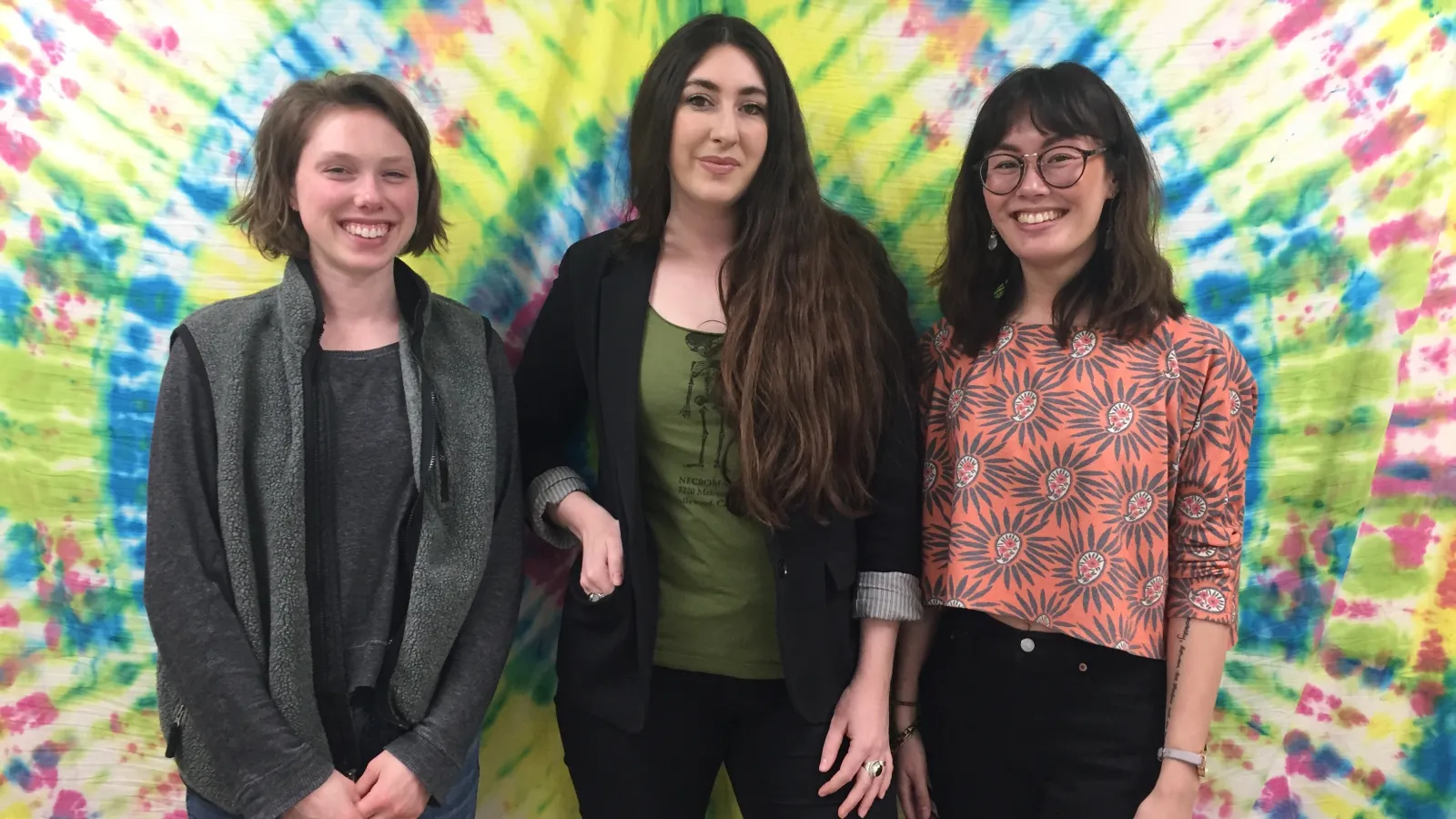 Haley (far left), Whitney (center), and Katie (far right) pose in front of a tapestry in a room in the Recovery Council on the group's last day.