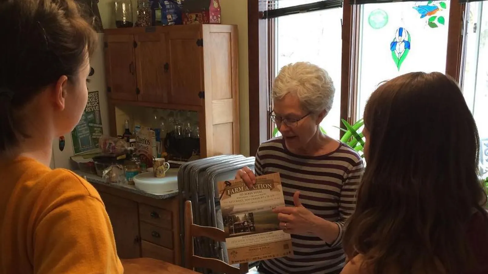 Barb shows Emily (L) and Ashley (R) a photo of the auction of Lenora and Jacob’s farm. 