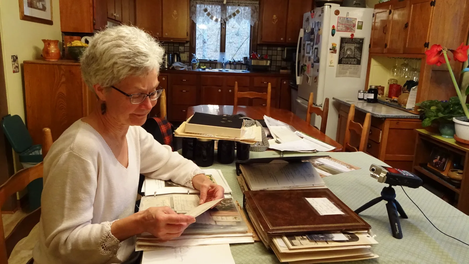Barb Bradbury sitting amidst documents, photos, and ephemera in her kitchen.