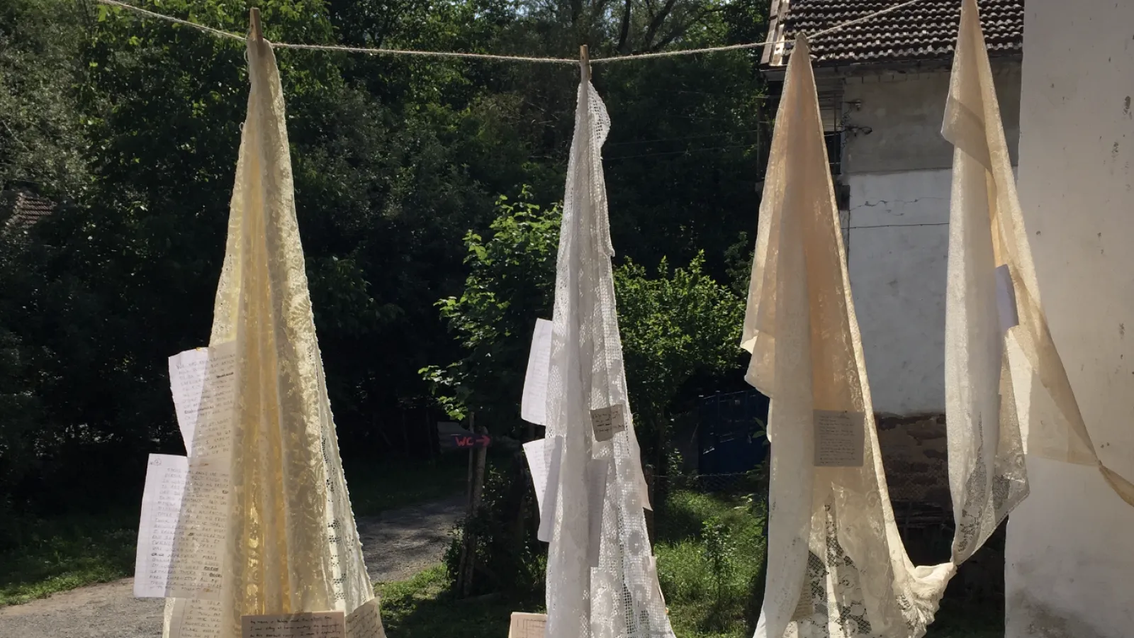Lace shawls hanging on a line with paper attached to them