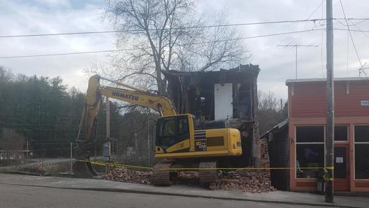 An excavator demolishes the rest of the Hughes Building, exposing the second story windows.