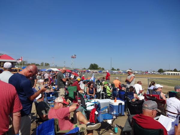 Attendees sit in portable chairs along the top of the track near the backstretch, some consulting race program booklets