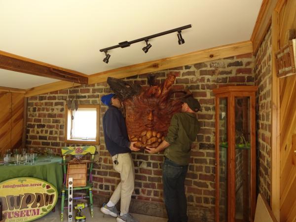 Andrew Mehall and Ross DiPenti hanging a wooden pawpaw carving on the wall of the soon-to-be Pawpaw Museum