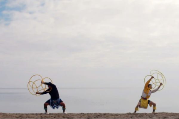 Two people on a beach with a big sky holding hula hoops