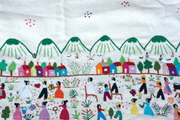 An embroidered folk art scene of dozens of people in a field in front of mountains