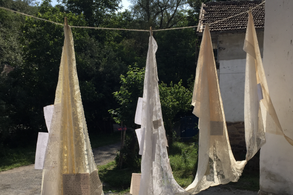 Image of lace shawls hanging on a line with paper attached to them.