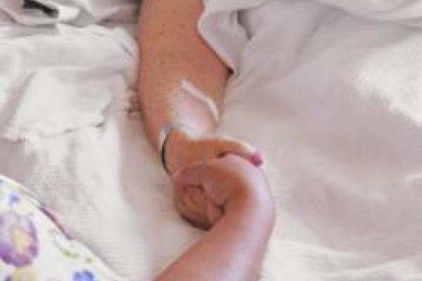 Elderly hospital patient holding hand of nurse