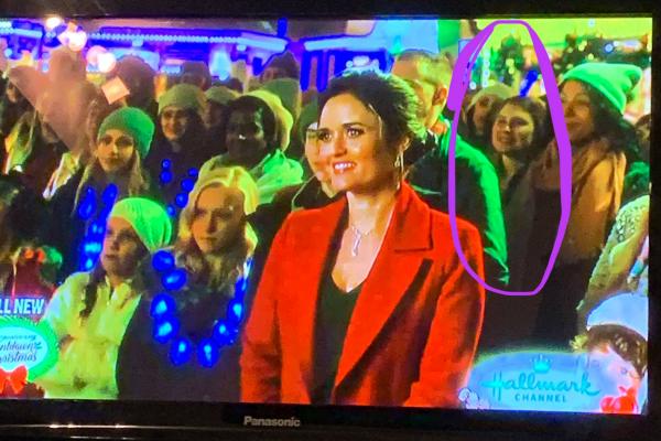 Varajon in 'Christmas in Dollywood' television movie. Photo of a television screen with a crowd of people at Dollywood. Varajon outlined in a circle.