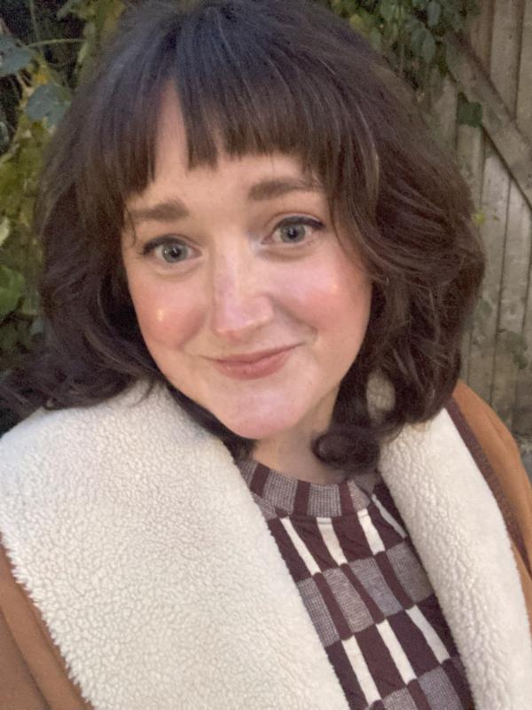 Emily Bianchi looking at the camera while wearing a brown and white sweater with a coat over it.