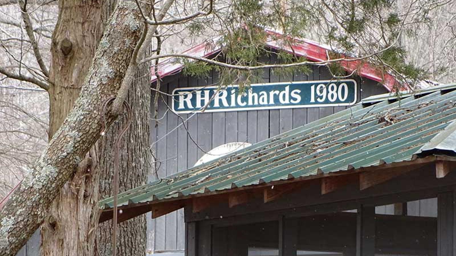 A sign on the front of Ronny’s grey barn that reads “RHRichards 1980” in white lettering on a green background. 